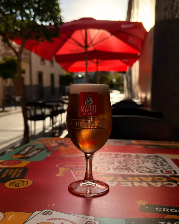 Copa de cerveza sobre una mesa de la terraza, con sombrillas rojas al fondo