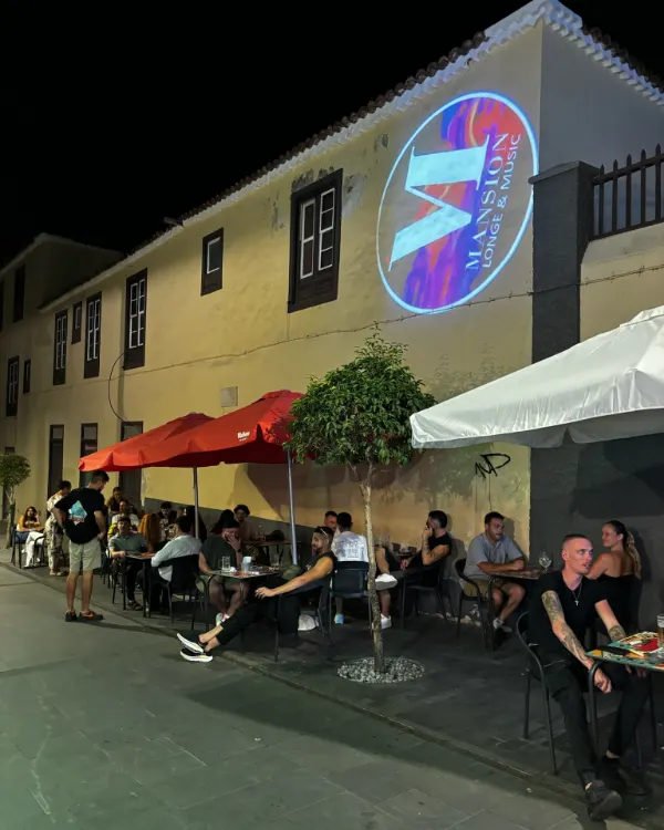 Terraza de De Locos de noche, con sombrillas rojas y clientes en las mesas