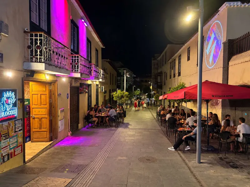 Fachada de De Locos con su neón y la terraza llena de gente por la noche